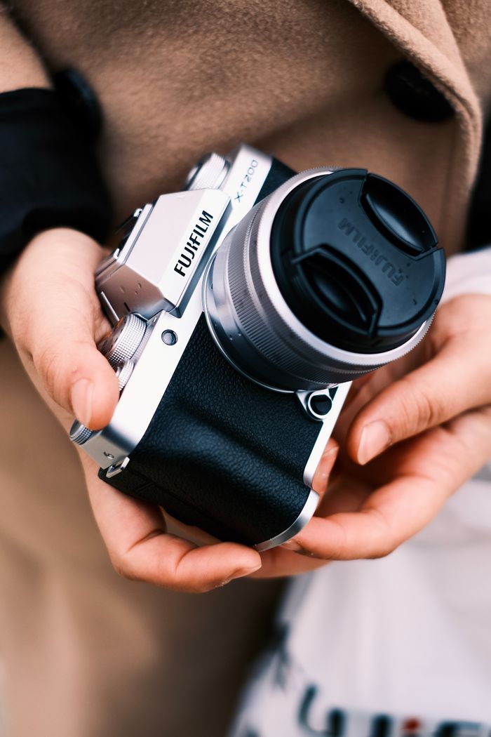Detailed shot of hands holding a silver Fujifilm camera, showcasing photography gear.