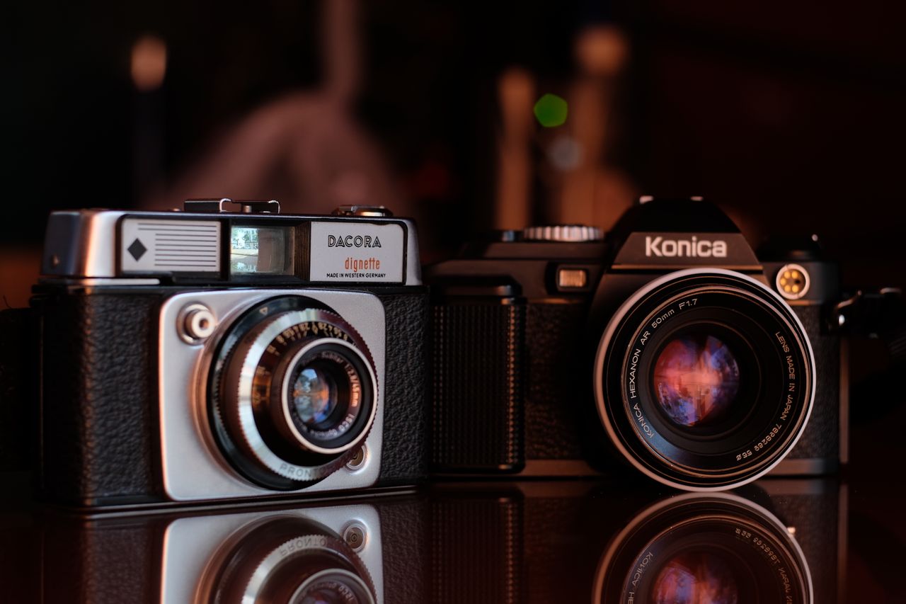 Close-up image of vintage Dacora Dignette and Konica cameras with reflections on surface.