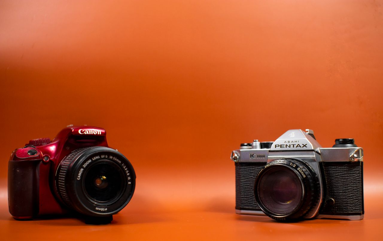 Vintage Pentax and Canon cameras displayed against an orange background, showcasing photography equipment.